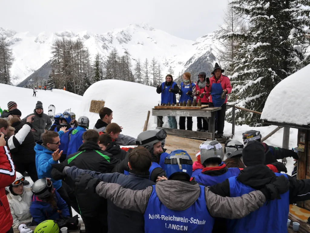 Große Gruppe steht im Kreis vor einer Hütte.
